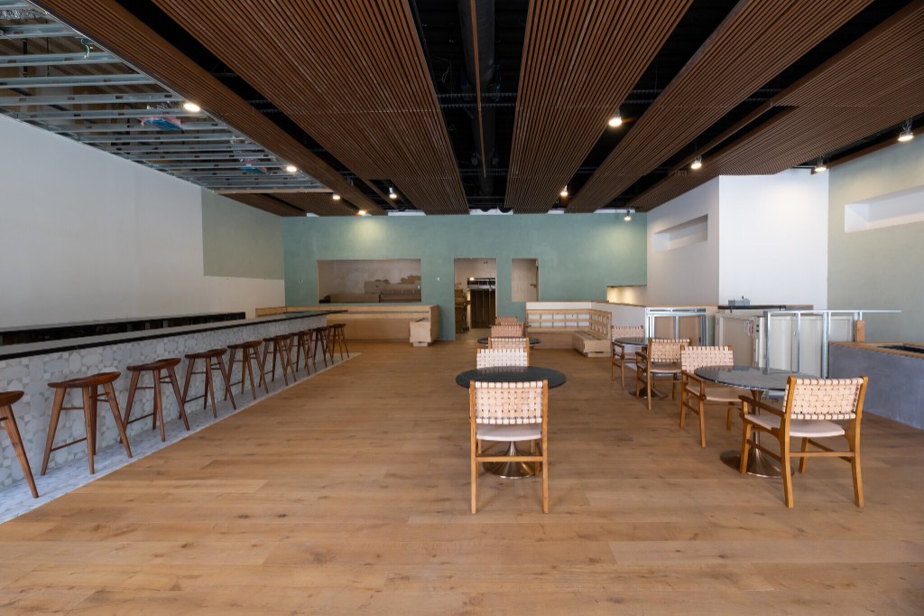 Interior of a modular café activation in vacant Los Angeles retail: wood-slat ceiling, sage walls, bar with patterned tile, and bistro seating.